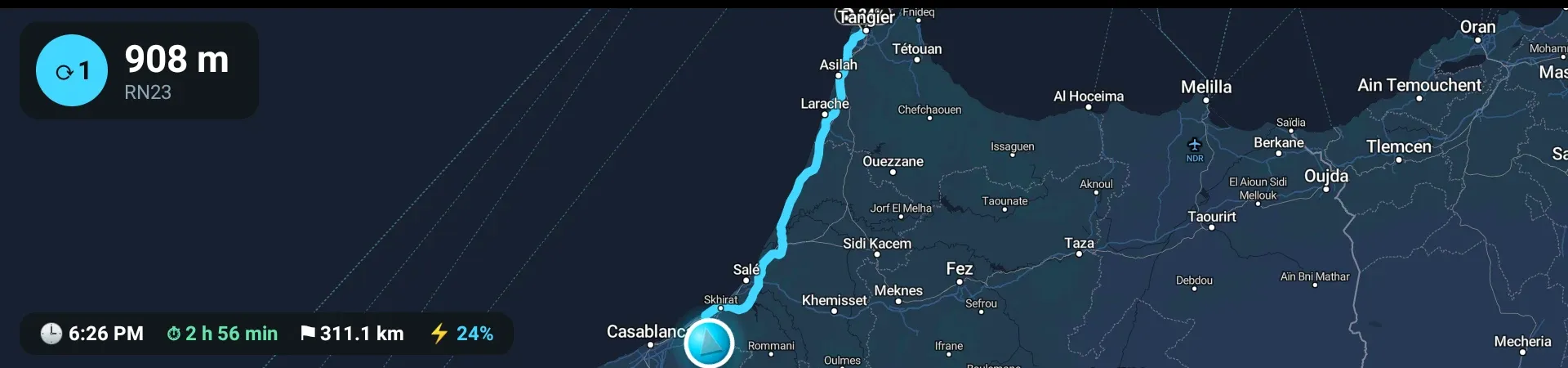 The instrument cluster behind the wheel showing the planned route the full length of the country, a roundabout card reading 908 m onto RN23 with its exit number, and a bar with arrival time 6:26 PM, 2 hours 56 minutes, 311.1 km remaining and 24 percent battery on arrival.